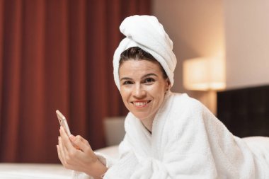 Bornoz istimal hareket eden telefon, duş aldıktan sonra rahat otel odasında yatan genç kadın