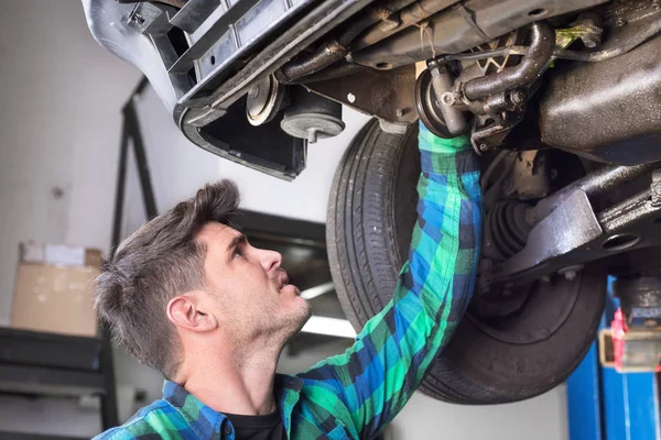 Handsome car mechanic checking suspension system of a lifted car at repair service station.