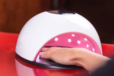 UV lamba Jel Lehçe manikür süreci tırnak salonu. Kadın eli yakın çekim.