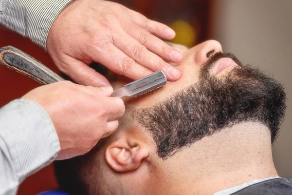 Knappe man met een scheerbeurt met vintage scheermes in de barbershop. — Stockfoto