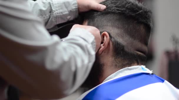 Bonito homem barbudo recebendo corte de cabelo por cabeleireiro na barbearia . — Vídeo de Stock