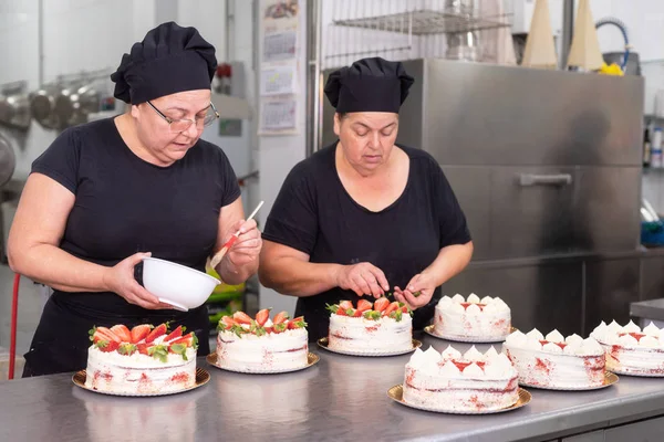 Two woman pastry chefs working together making cakes at the pastry shop.