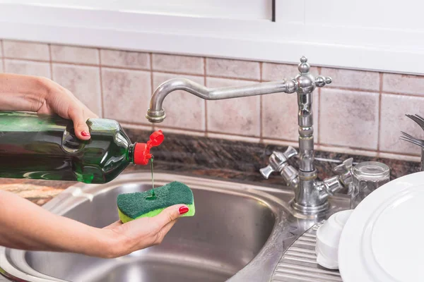 woman with red manicure putting detergent in the scourer, to wash the dishes.