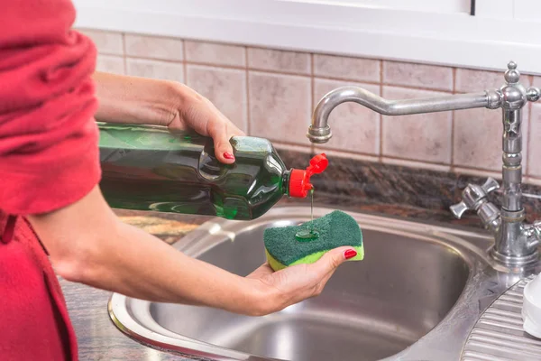 Vrouw met rode manicure wasmiddel aanbrengend het vlies, de afwas. — Stockfoto