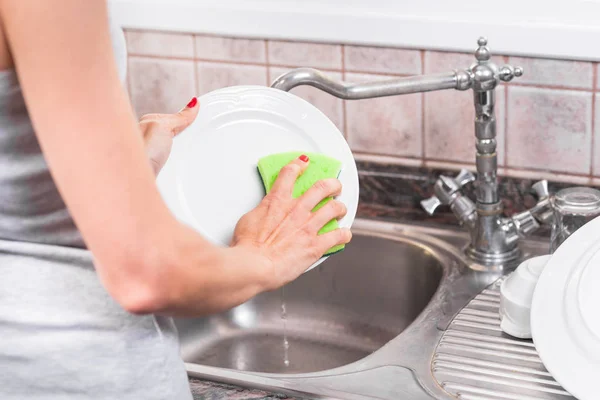 Young woman with red manicure, washing dishes in the sink of the kitchen. — Stock Photo, Image