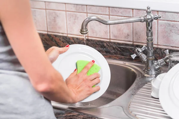 Jonge vrouw met rode manicure, afwas in de gootsteen van de keuken. — Stockfoto