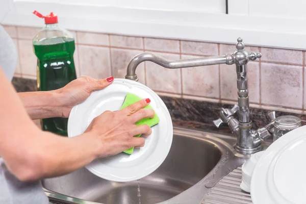 Junge Frau mit roter Maniküre spült Geschirr in der Küchenspüle. — Stockfoto