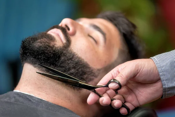 Knappe man met een scheerbeurt met een schaar in de barbershop. — Stockfoto
