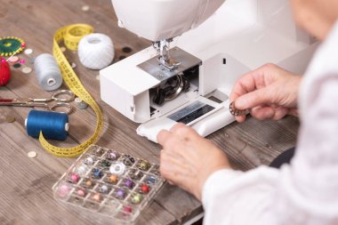 Bir elektrikli dikiş makinesinin bakımını yapmak için bobin kılıfı kaldırarak kıdemli kadın terzi elleri yakın çekim.