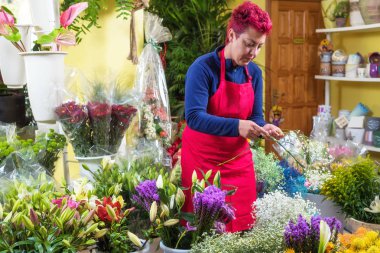 Mutlu kadın çiçekçi, düzenlemeler yapma ve kameraya gülümseyerek. küçük işletme Çiçekçi dükkanı sahibi.