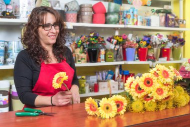Gülümseyen olgun kadın çiçekçi çiçekçide bir buket çiçek yapıyor..