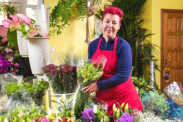 Mutlu kadın çiçekçi, düzenlemeler yapma ve kameraya gülümseyerek. küçük işletme Çiçekçi dükkanı sahibi.