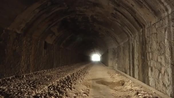 POV wandelen binnenkant van oude donkere lange verlaten tunnel met fel licht in het einde. — Stockvideo