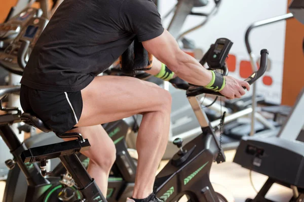 Spor salonunda kaslı adam bisiklet, kardiyo egzersiz bisiklet bisiklet yapıyor bacaklar egzersiz, sınıf iplik.
