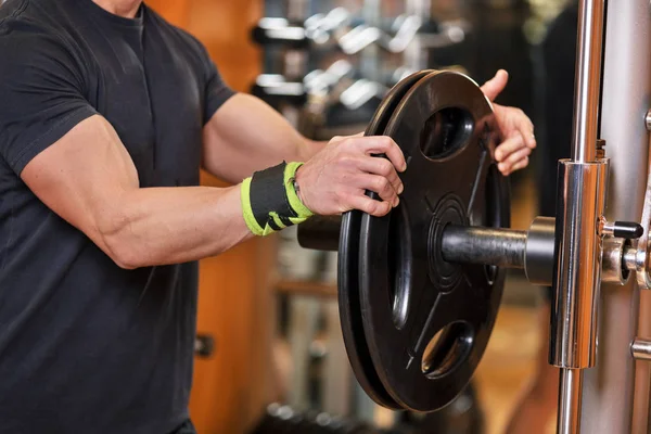 Close-up shot van niet-identificeerbare gespierde man oppakken van zware halter gewichten van apparatuur rack in moderne sportschool. — Stockfoto