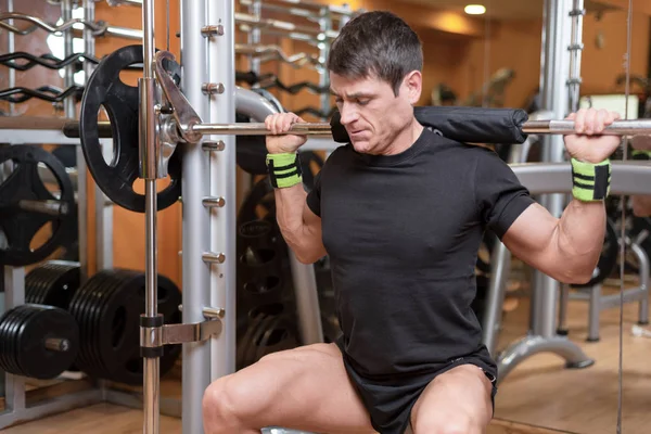 Sport, bodybuilding, lifestyle and people concept - young man with barbell doing squats in gym. — Stock Photo, Image