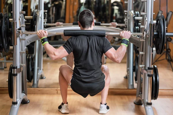 Sport, bodybuilding, levensstijl en mensen concept - jonge man met barbell doen squats in gym. — Stockfoto