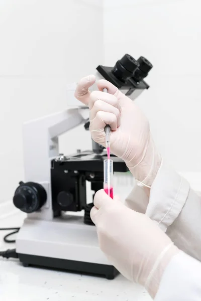 Tubo de teste de enchimento do cientista com pipeta no laboratório. Visão de perto de um tubo de ensaio de enchimento de cientista fêmea com pipeta por microscópio no laboratório . — Fotografia de Stock