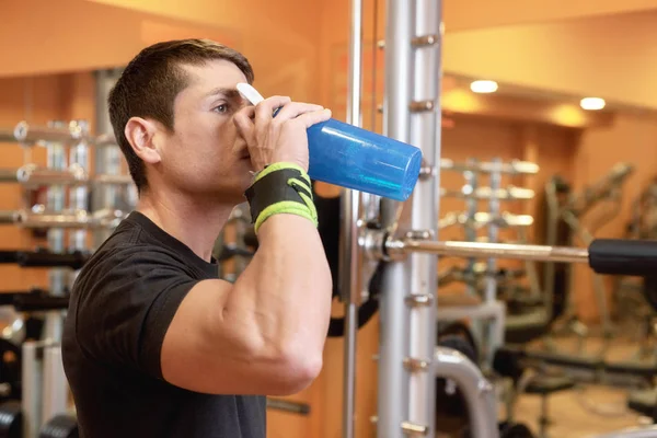 Spierman drinkt water uit blauwe fles in de sportschool. — Stockfoto