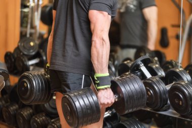 spor salonunda ağır dambıl tutan kaslı adam yakın.