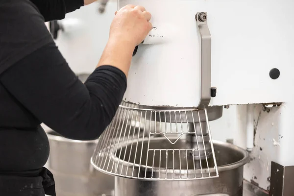 Confectionery factory worker standing and operating industrial dough mixer machine.