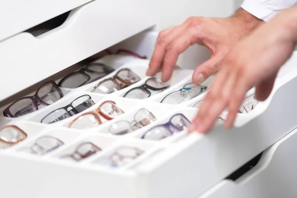 Руки офтальмолога закрываются, выбирая очки из ящика в оптическом магазине. — стоковое фото