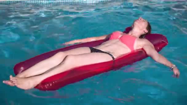Молодая счастливая женщина отдыхает на надувной игрушке в голубом бассейне в солнечный день . — стоковое видео