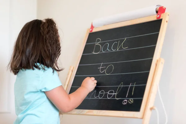 Cute little schoolgirl writing in chalkboard with text back to school. — Stock Photo, Image