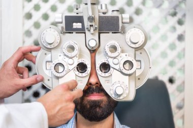 Optimetrist klinikteki erkek hasta için görüş testi yapıyor. Erkek göz doktoru, optometrist deneme çerçeveli hasta adamı muayene ediyor.. 
