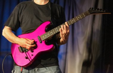 Sahnede pembe elektro gitar çalan müzisyen.