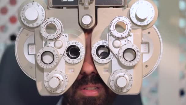 白いコートで眼科医のクローズアップショットは、ポロプター器具のレンズを交換し、眼科検査を受けている男性患者と話す. — ストック動画