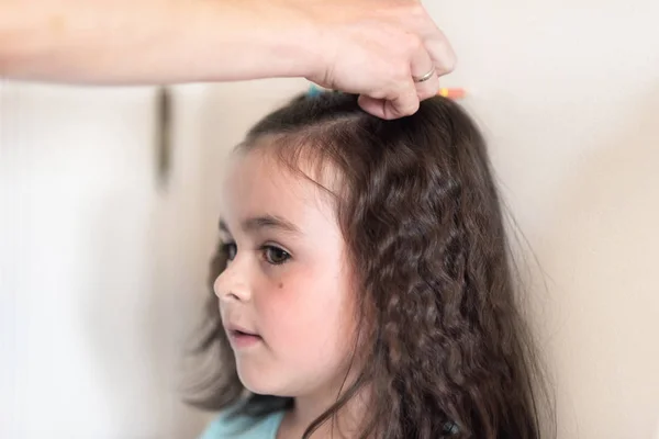 Mother measuring height of her daughter near white wall.