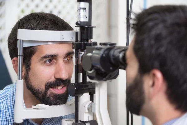男性医生眼科医生正在检查在现代诊所中英俊的年轻人的眼视力。眼科诊所的医生和病人. — 图库照片