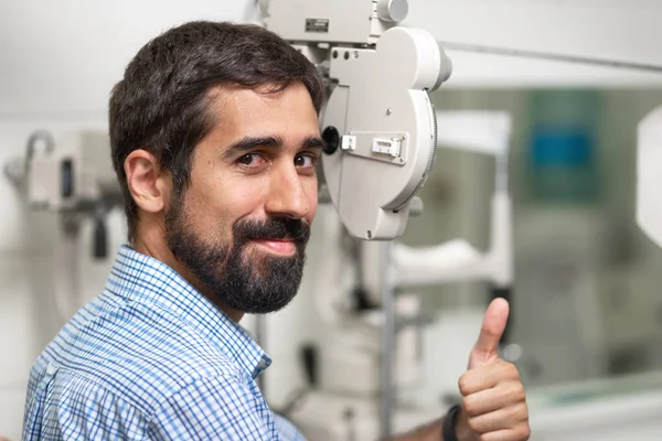 Patient in modern ophthalmology clinic checking the eye vision, showing thumb up.