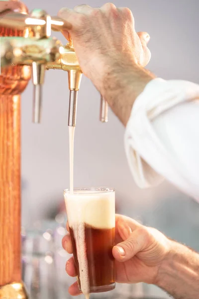 Verter cerveza para el cliente. Cantinero vertiendo cerveza mientras está de pie en el mostrador del bar . — Foto de Stock