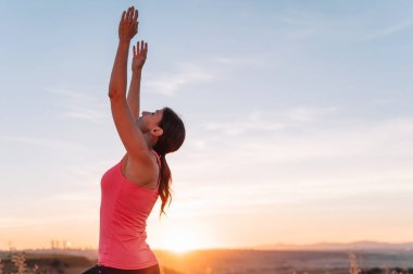 Kadın dışarıda yoga yapıyor, güzel havanın ve doğada pozitif enerjinin tadını çıkarıyor..