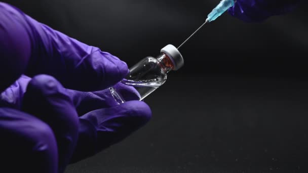 Close-up van de handen van de arts die de spuit en injectieflacon klaarmaken voor vaccinatie op een zwarte geïsoleerde achtergrond. — Stockvideo