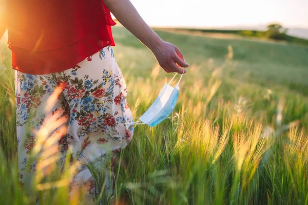 Close up of unrecognizable woman walking outdoors throwing away her mask. Young happy girl removing protective mask. End of pandemic coronavirus concept. Meadow landscape, Pollen allergy at spring. — Stock Photo, Image