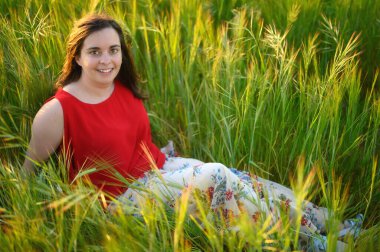 Kırmızı elbiseli, yeşil çayırda uzanmış güzel bir genç kadın. Açık havada. Doğanın tadını çıkarıyorum. Yeşil bahar mahsulünde gülümseyen. 