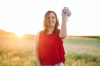 Yazın gün batımında çayıra spor ayakkabısı fırlatırken gülen neşeli genç bir kadın..