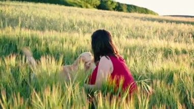 Gün batımında çayırda köpeğiyle oynayan neşeli genç bir kadın. Baharda eğlenceli bir golden retriever 'ın sinematik videosu.