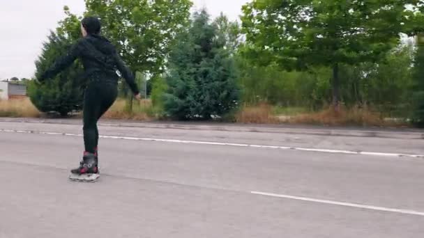 Volg schot, zijaanzicht van jonge vrouw oefenen rolschaatsen op de weg. — Stockvideo