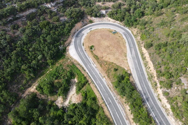 Aerial view of winding road in high mountain pass trough green pine woods.