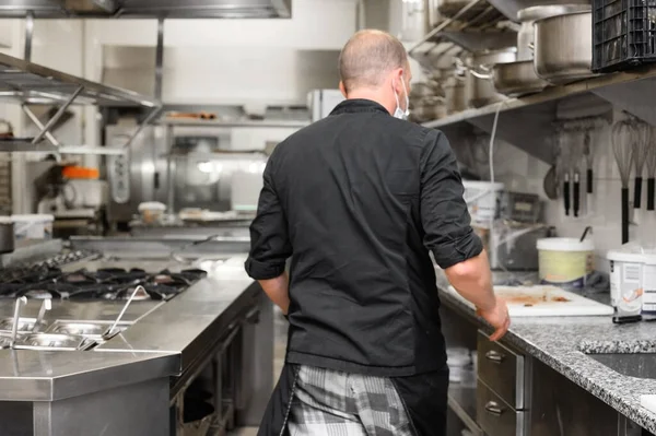 Chef in uniform cooking in a commercial kitchen. Male cook wearing apron standing by kitchen counter preparing food. — Stock Photo, Image