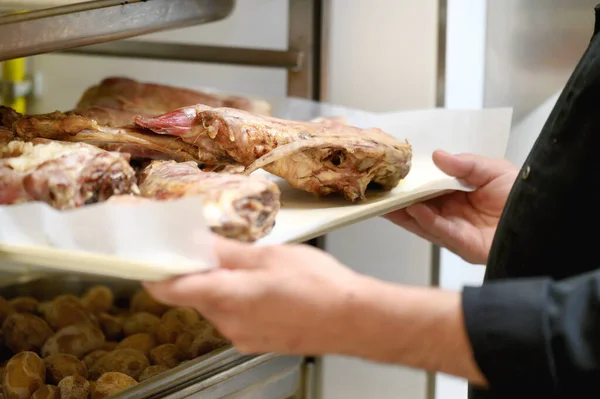 Unrecognizable chef putting baking tray with meat into rack in commercial kitchen. — Stock Photo, Image