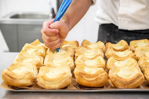 Pastry chef decorates biscuit tartlet with cream from pastry bag close-up