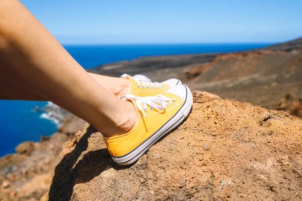 Kvinnan slappnade av och njöt av landskapet. Resenären sitter på Rock i gula gympaskor. Sommarlov. Närbild. — Stockfoto