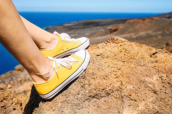 Kobieta zrelaksowana, ciesząca się krajobrazem. Podróżnik siedzący na skale w żółtych trampkach. Wakacje. Zamknij się.. — Zdjęcie stockowe