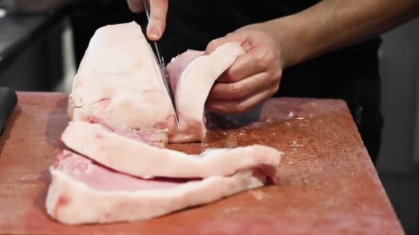 Свинячий стейк на дерев'яній дошці. Бучер зрізає сире м "ясо ножем у повільному русі. — стокове відео