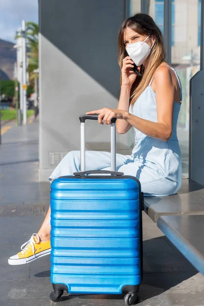 Koronavirová pandemie. Žena s obličejovou maskou během nového normálu, mluví po telefonu, zatímco čeká na veřejnou dopravu. — Stock fotografie